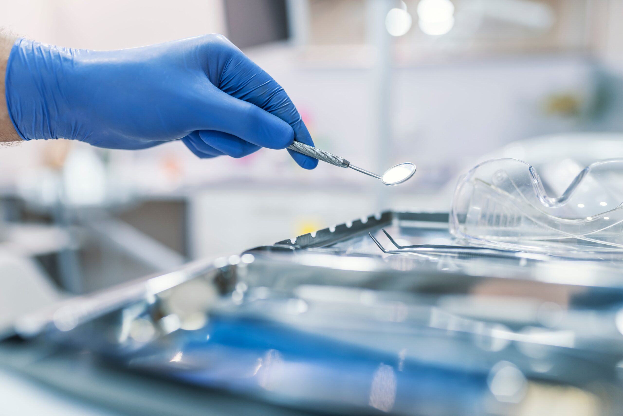 A gloved hand holds a dental mirror above a tray of sterilized dental instruments, indicating dental equipment maintenance in Fort Worth, TX and preparation for a dental examination.